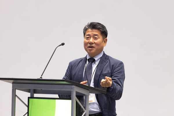 A man stands at a podium with a microphone and speaks to a large crowd gathered in a big auditorium.